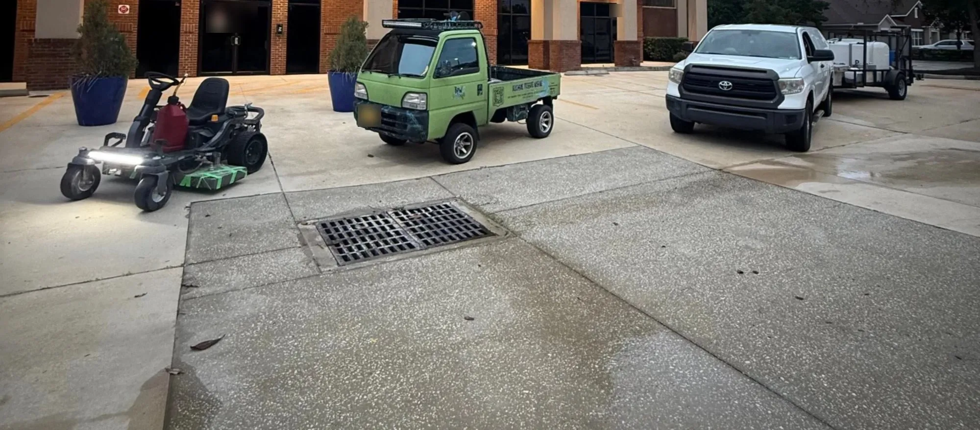 Beachside’s custom-built ride-on pressure washer, green Beachside utility truck, and a pickup with a wash trailer outside a commercial building at dusk