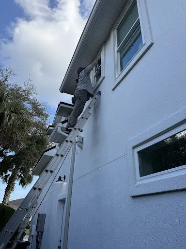 A crew member on a ladder cleaning second-story windows